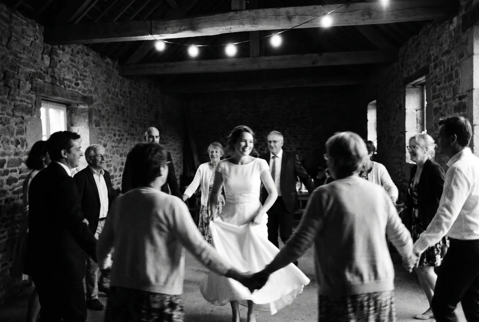 Invités de mariage dansant en ronde dans une grange en pierre, la mariée tourne au centre