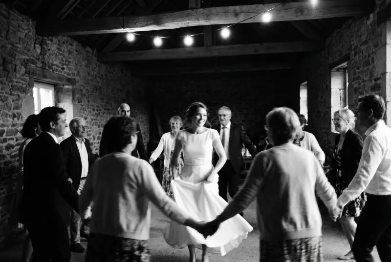 Invités de mariage dansant en ronde dans une grange en pierre, la mariée tourne au centre