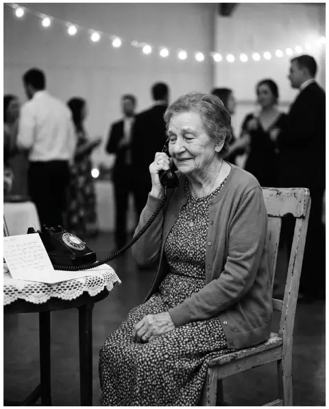 Une grand-mère assise parle avec émotion dans le combiné d'un téléphone à cadran lors d'un mariage