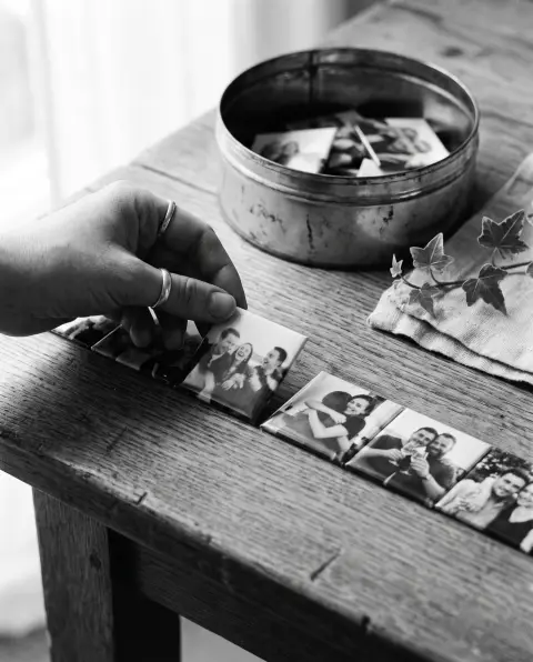 Une main pioche un magnet photo parmi une rangée de petits tirages d'invités posés sur une table en chêne