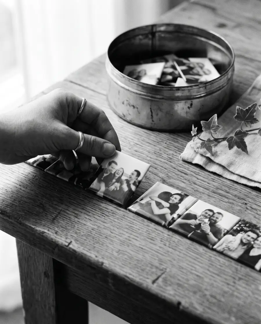 Une main pioche un magnet photo parmi une rangée de petits tirages d'invités posés sur une table en chêne